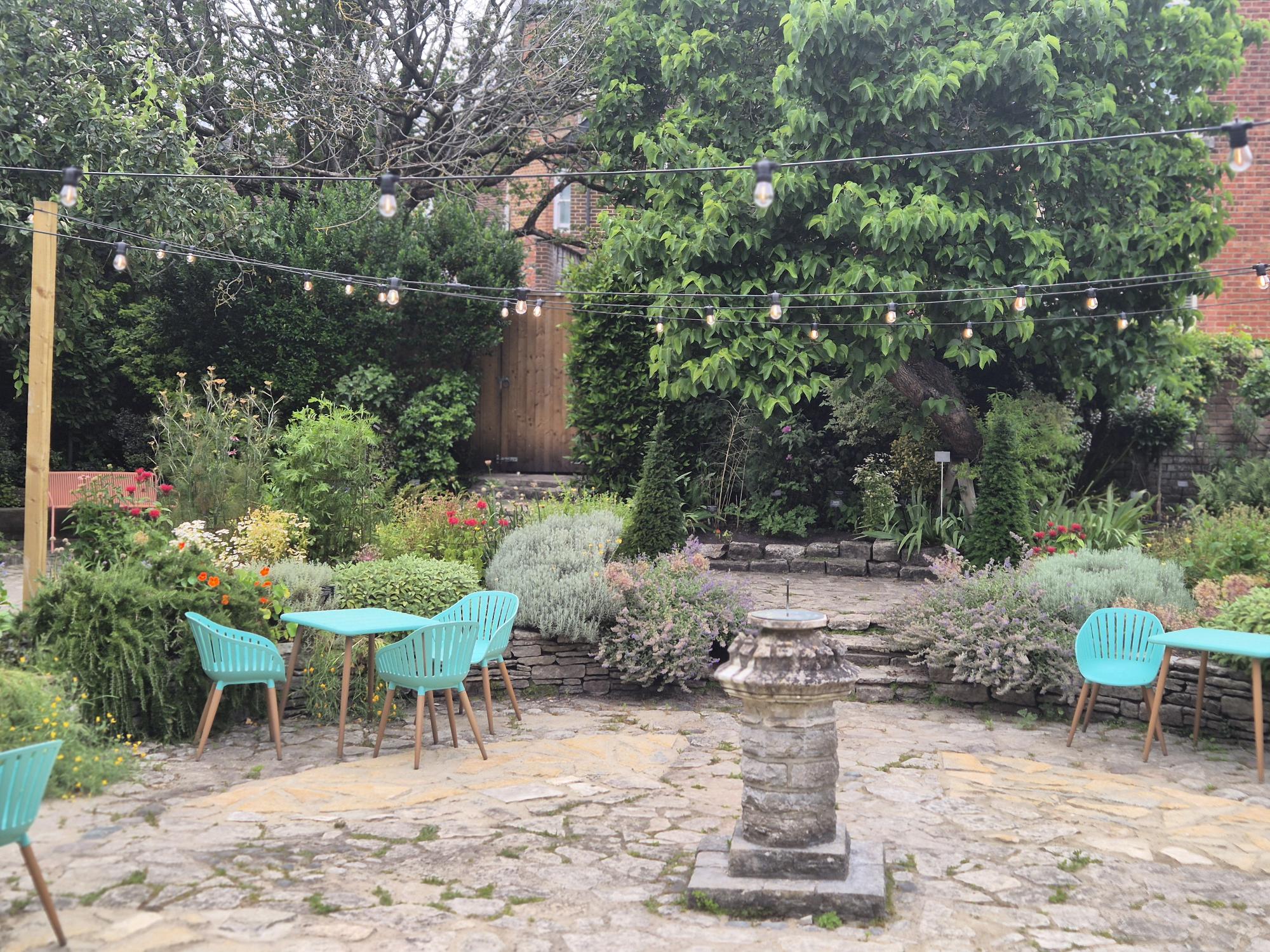 Scaplen's garden with festoon lights, sundial, tables and chairs, greenery and trees